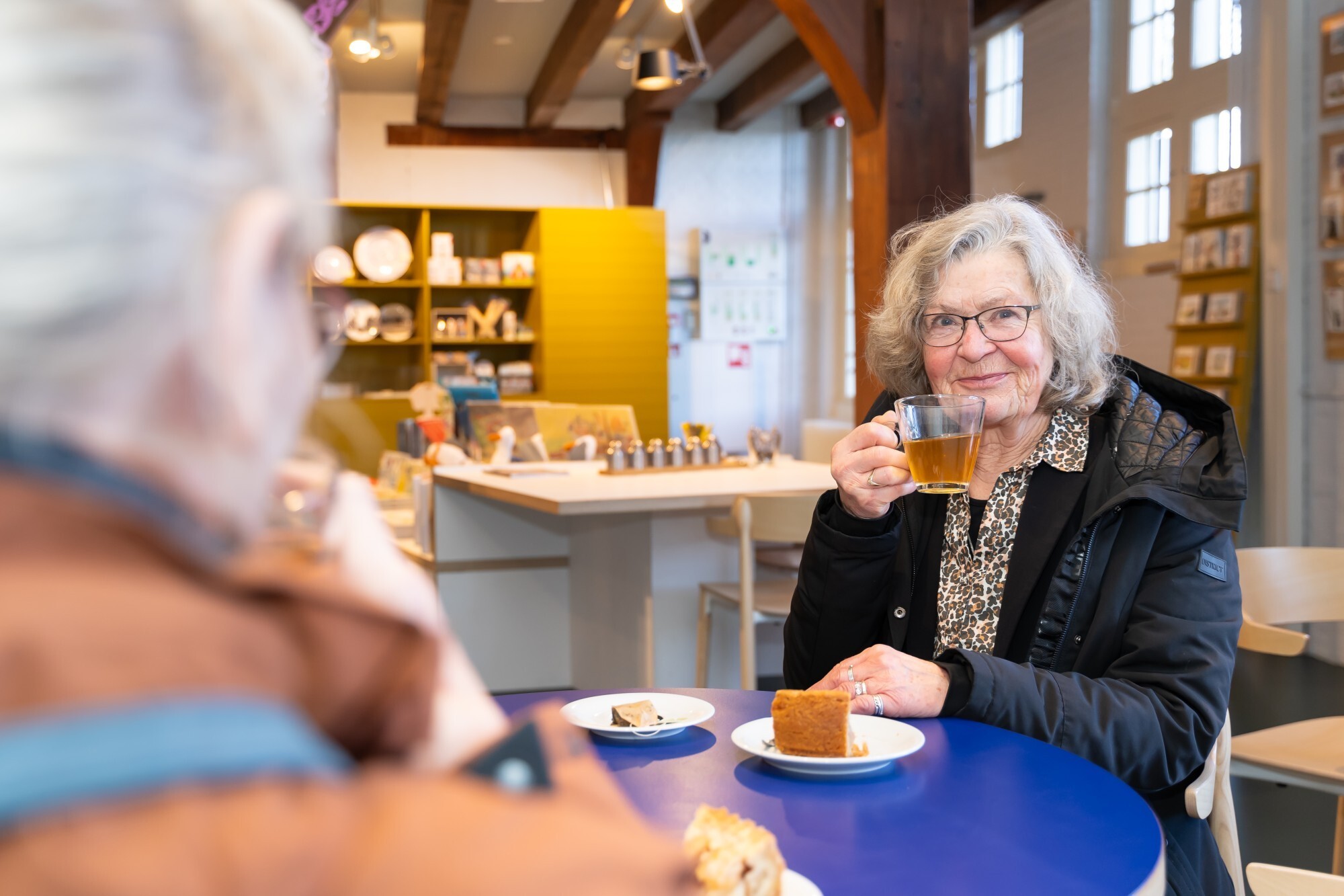 Een dame geniet van een kop thee met een stuk appeltaart voor zich