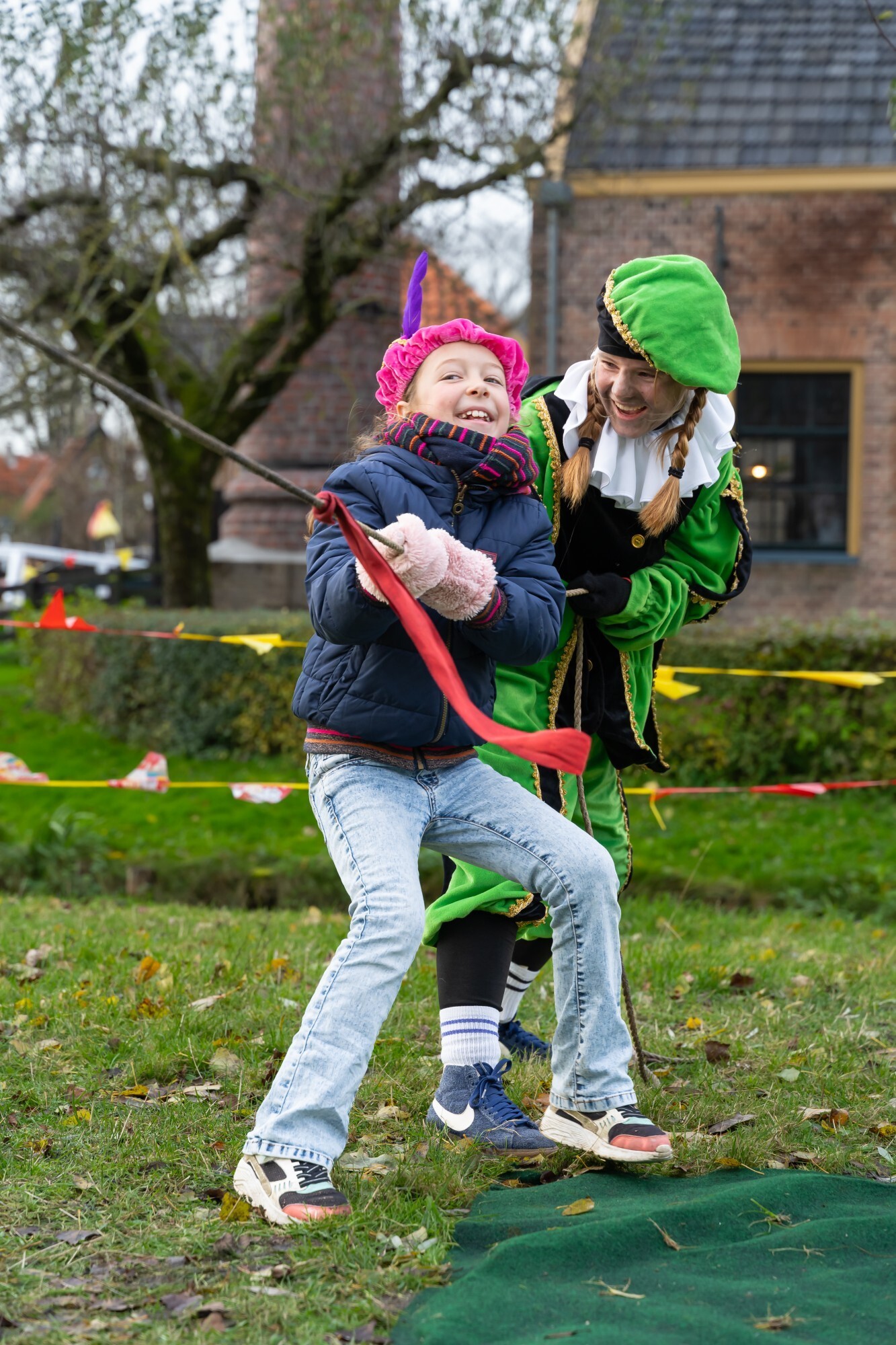 Foto van Pietendorp, waarbij een kind samen met een piet aan het touwtrekken is en plezier heeft.