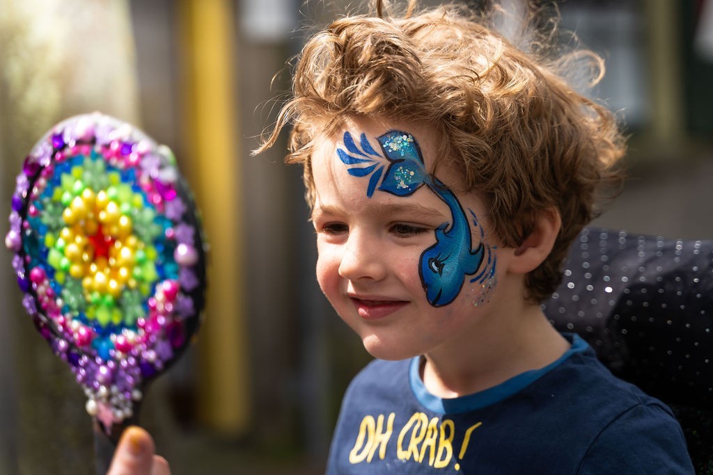 Jongentje die geschminkt is en in de spiegel kijkt
