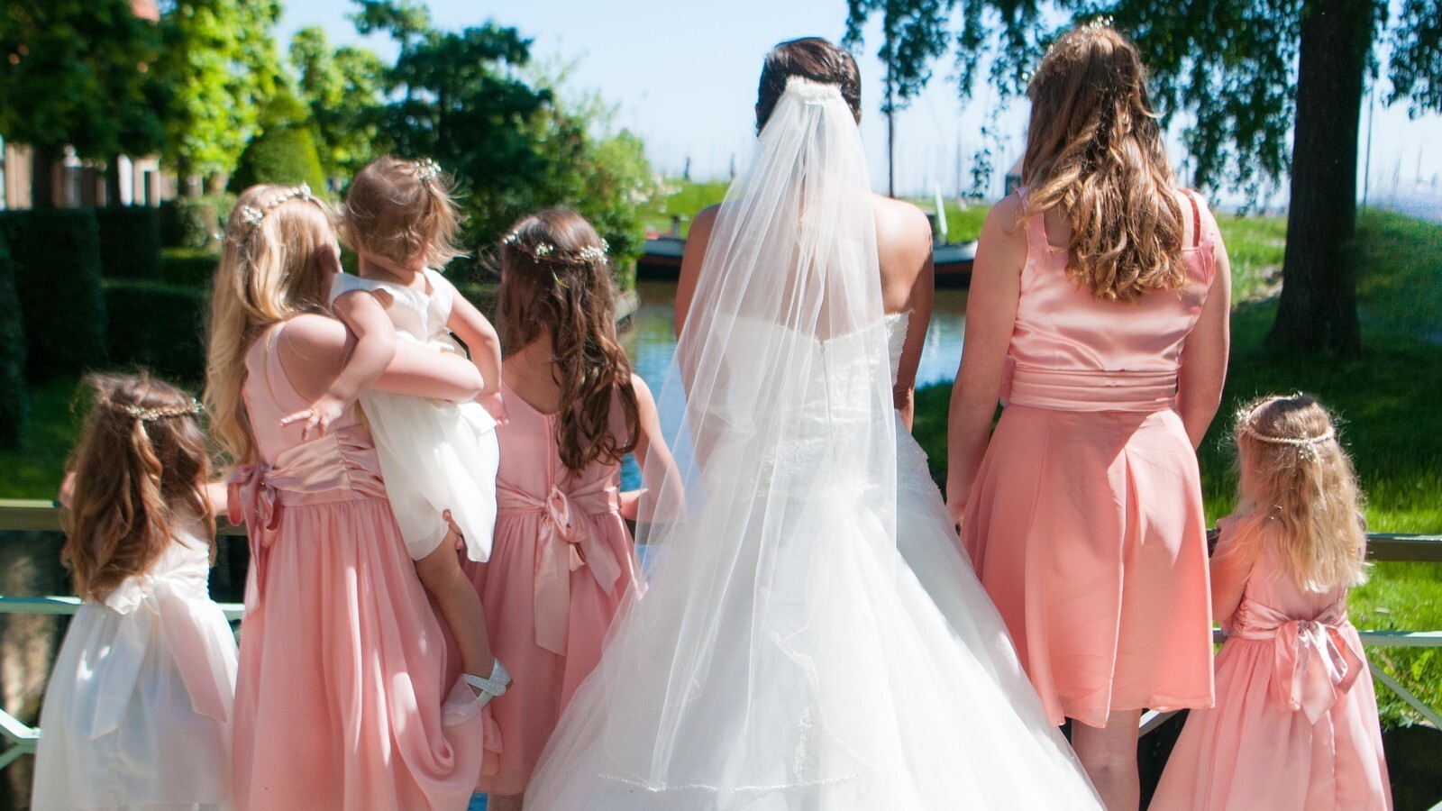 Een bruid en haar bruidsmeisjes kijken naar het water vanaf een brug