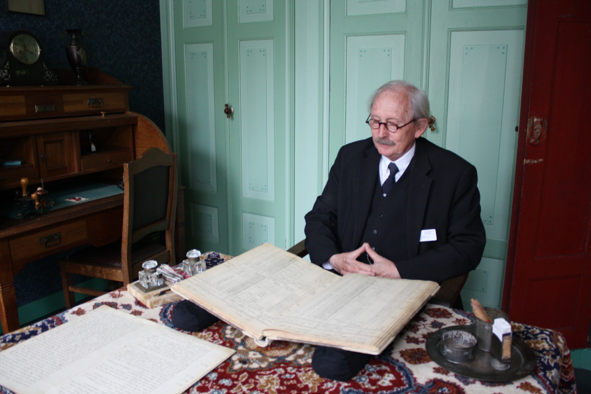 De rolspeler van de boerenleenbank, hij zit in het kantoor met een groot boek.