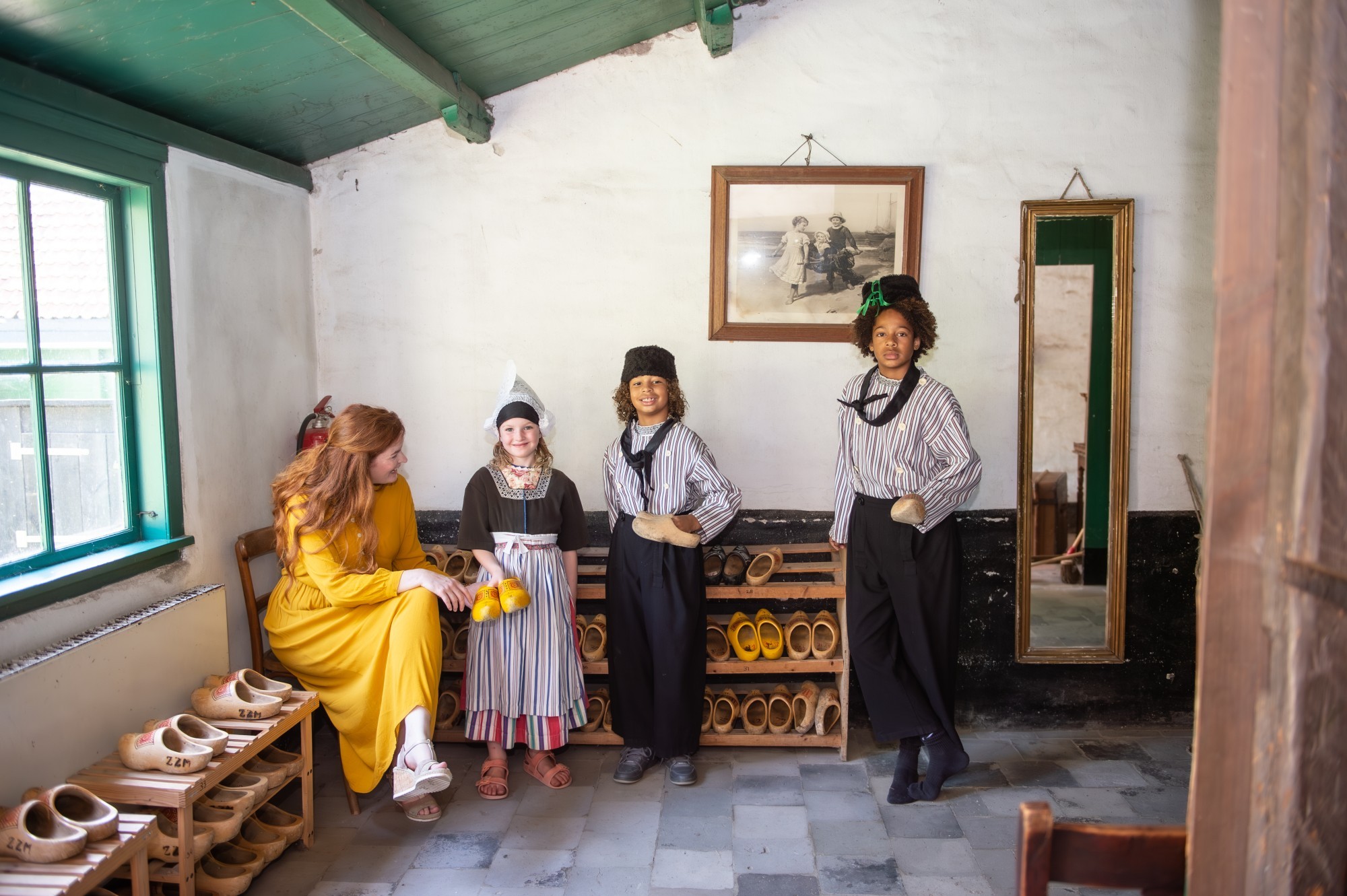 Drie kinderen en een vrouw staan bij een rek met klompen