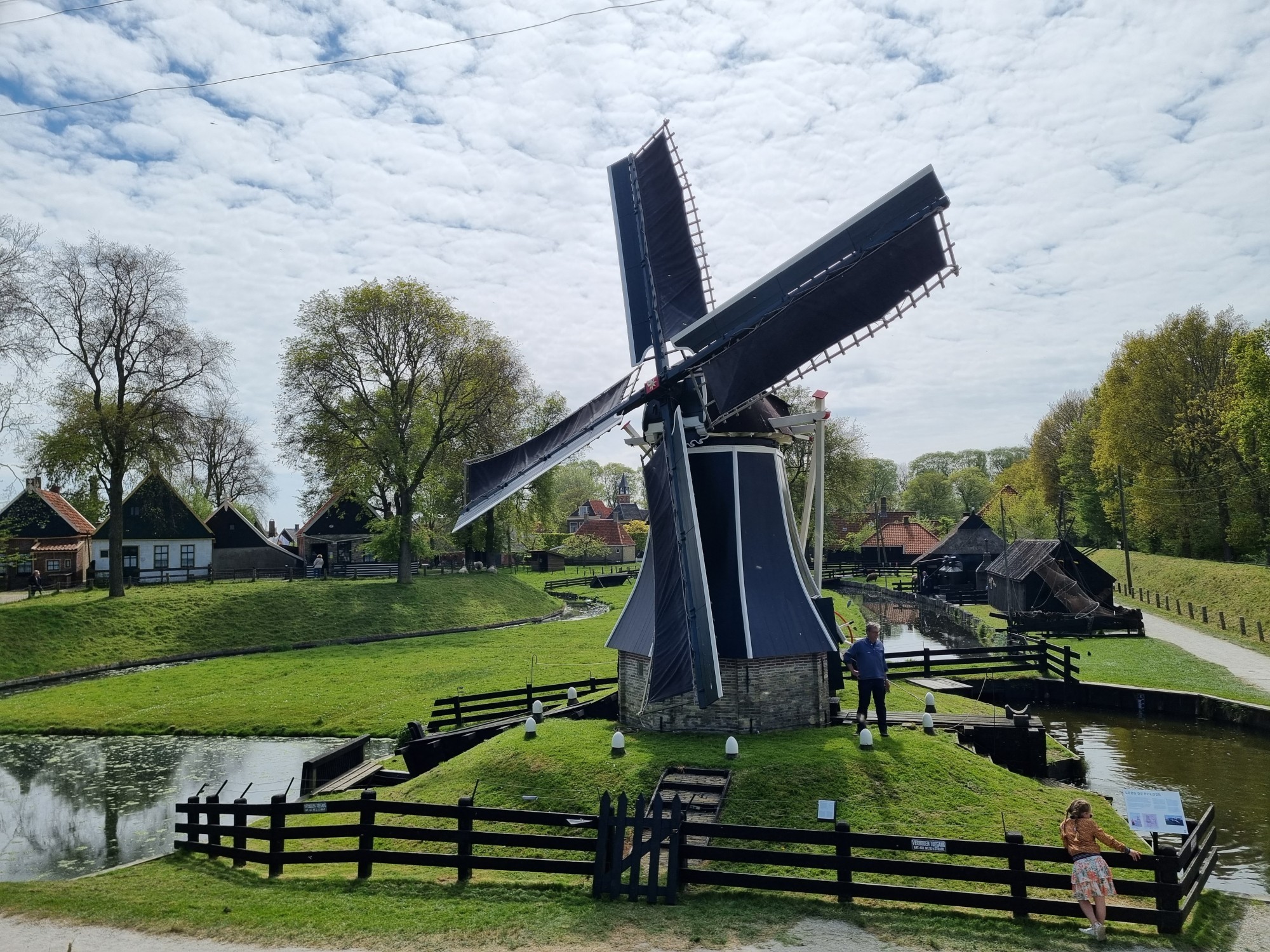 De molen vanaf de dijk gefotografeerd, er staan een meisje en een man bij.