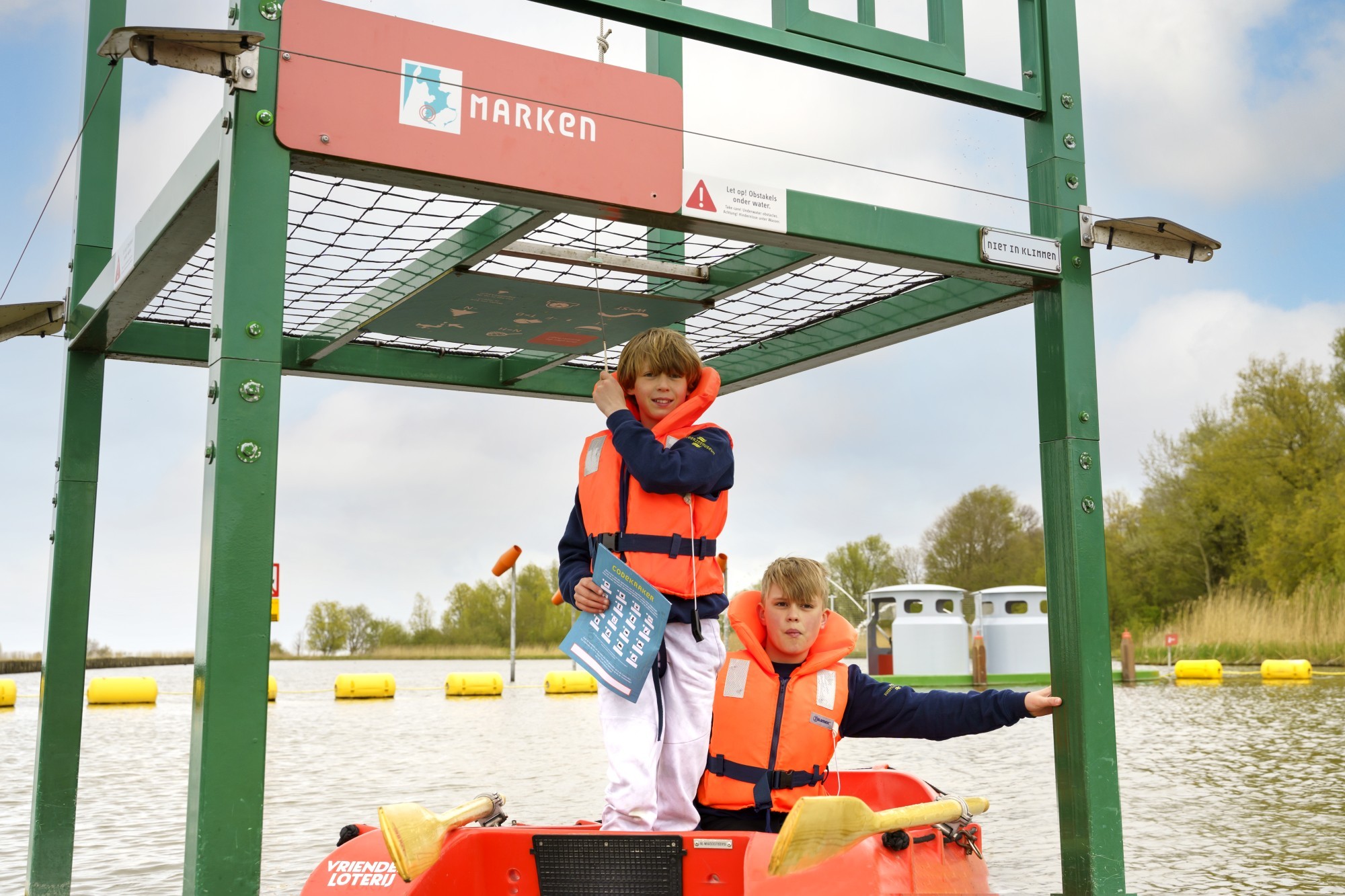 Twee jongens in een roeiboot, ze dragen oranje reddingsvesten.