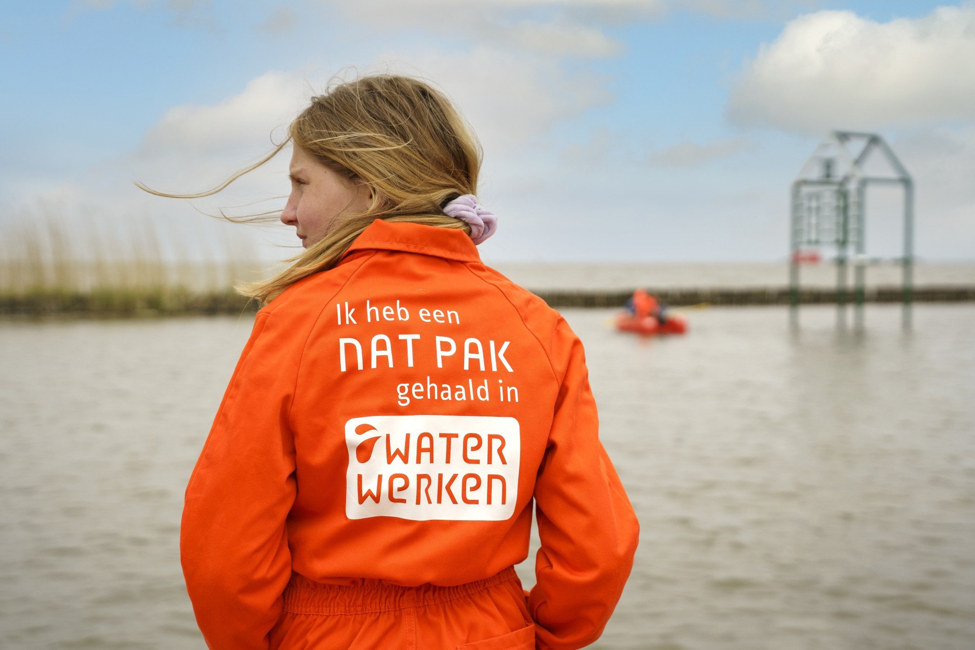 Een meisje draagt een oranje werkoveral met de tekst "ik heb een nat pak gehaald in waterwerken
