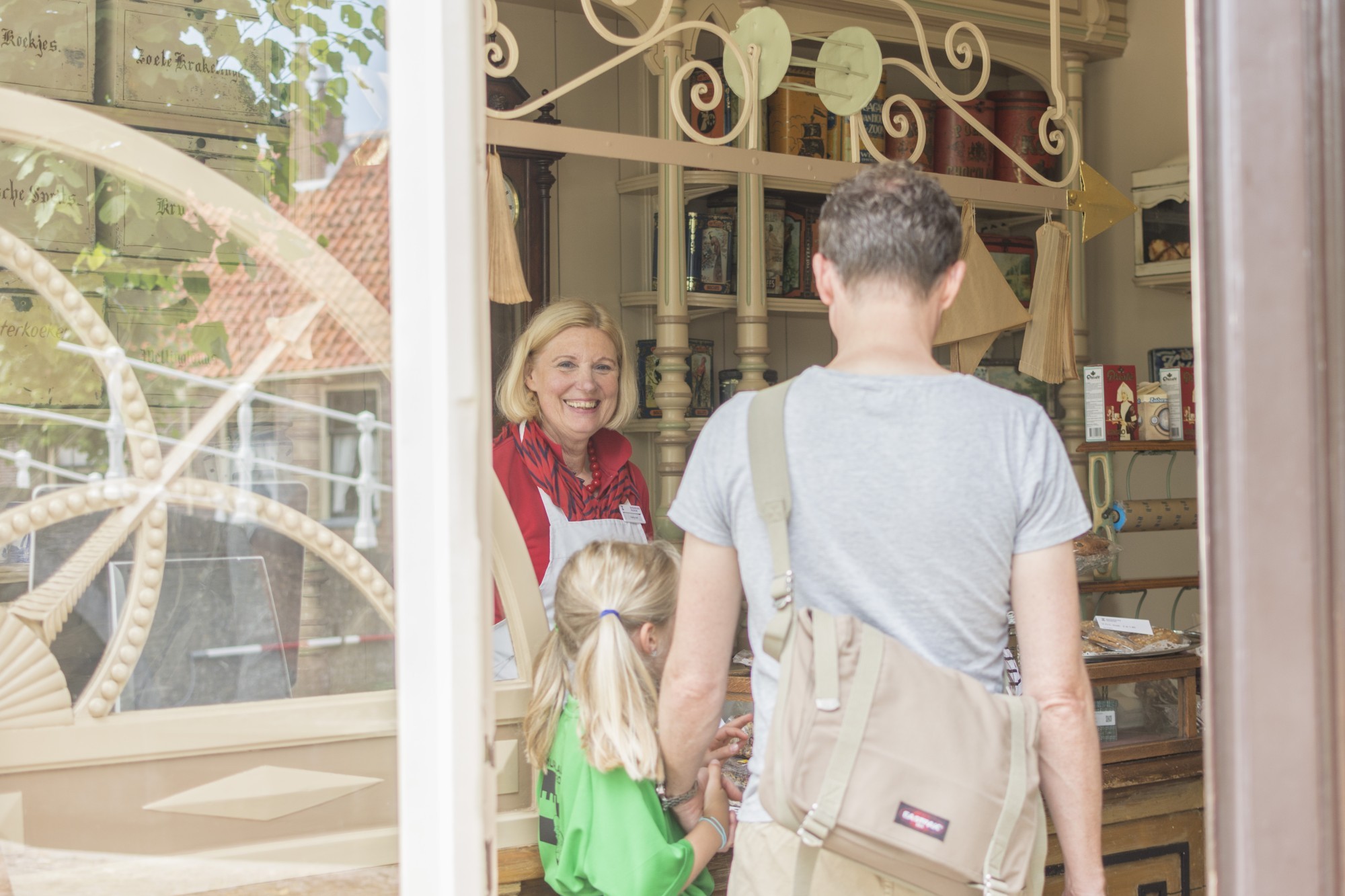 Een man en zijn dochter lopen de bakkerij binnen, waar een medewerker hen vriendelijk met een glimlach verwelkomt.