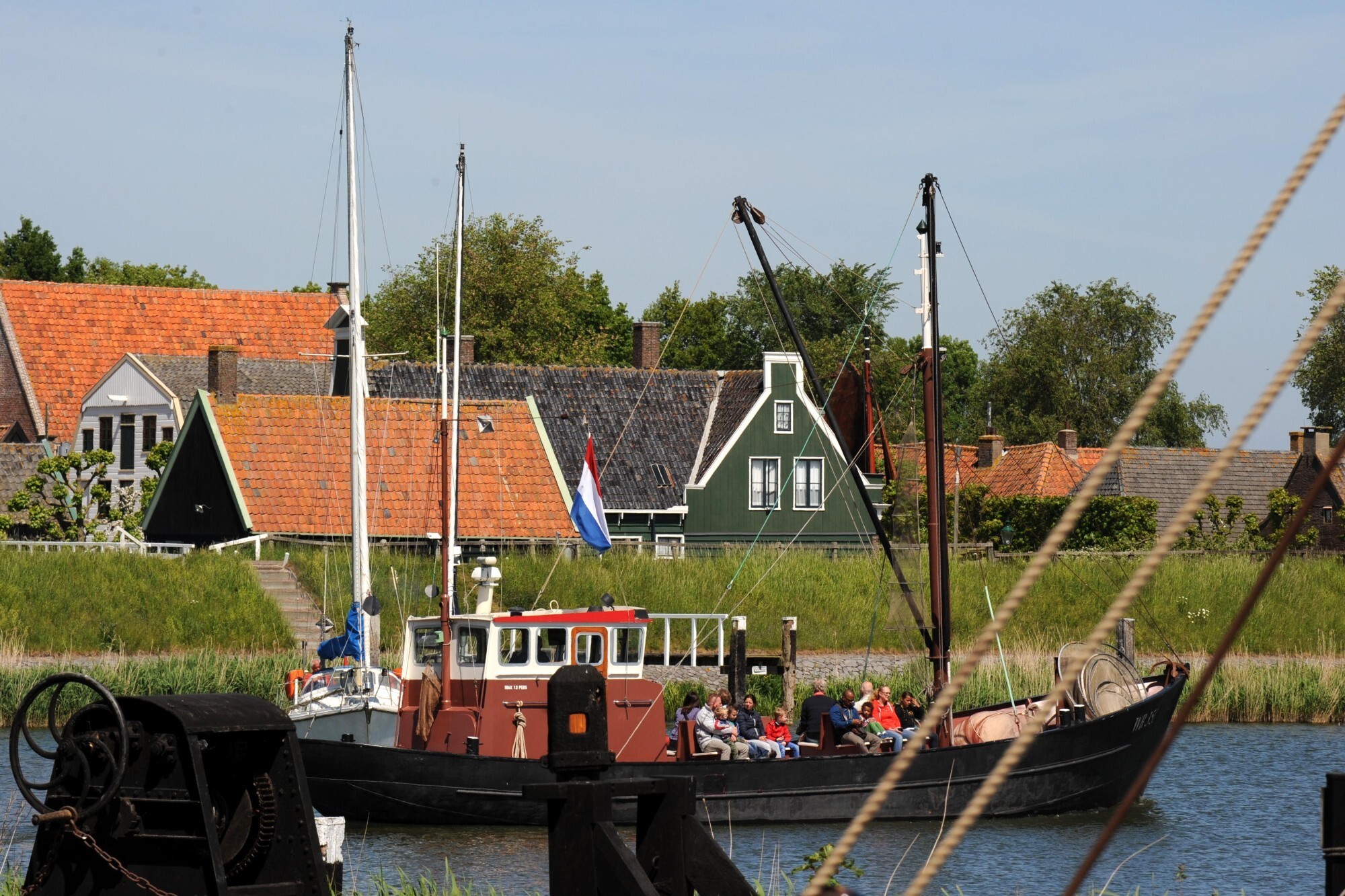Een traditionele vissersboot met passagiers vaart langs een typisch Zuiderzeedorp met karakteristieke huizen en groene omgeving