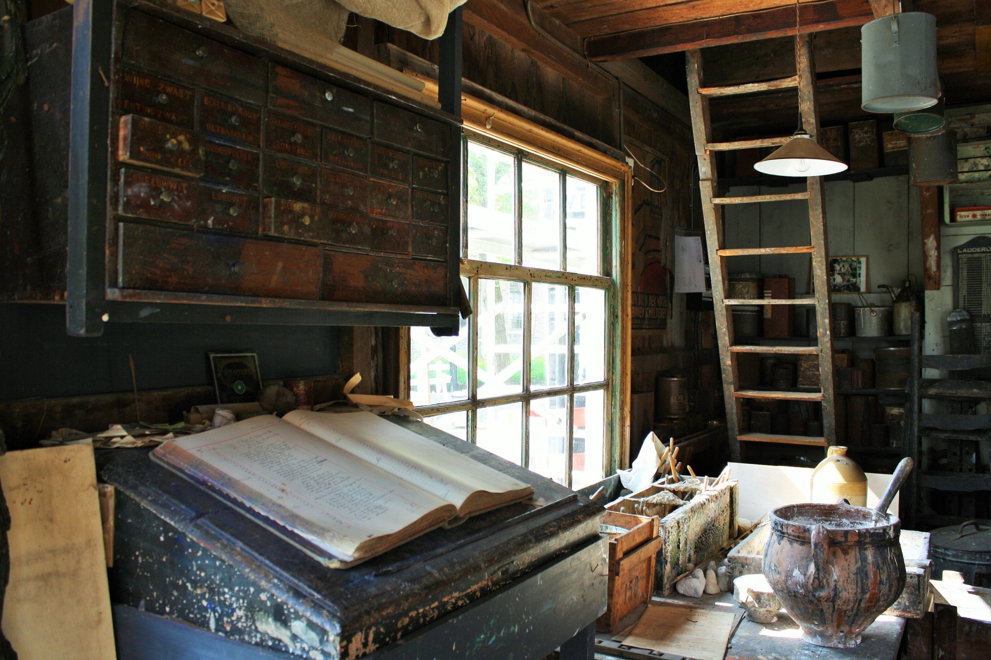 De schilderatelier van de binnenkant, een groot boek is opengeslagen en meerdere potten met verf staan in de achtergrond