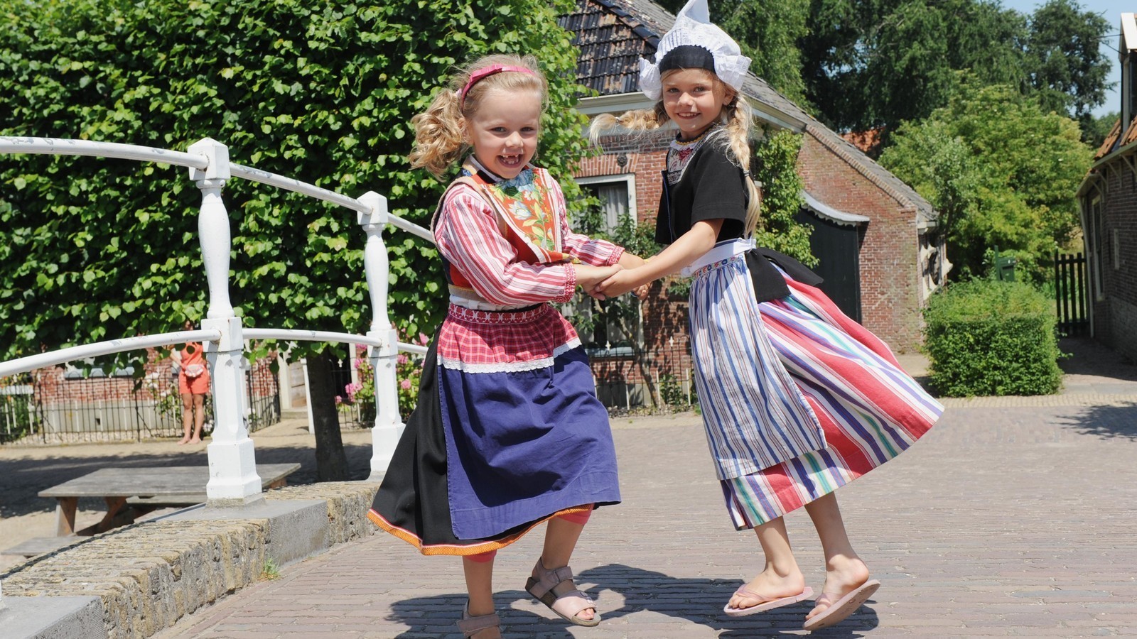 Twee meisjes in klederdracht springen hand in hand vrolijk op en neer.